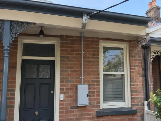 Brick house facade with new overhead service cable and point-of-attachment bracket above the eaves in Paddington