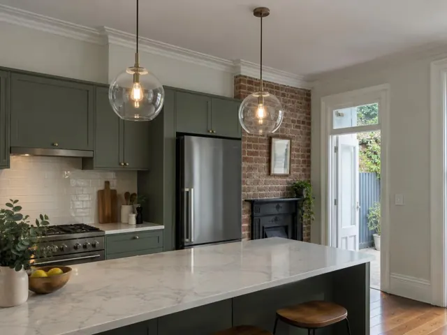 Kitchen with two glass pendant lights above a marble island in a green and brick interior in Woollahra